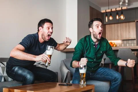 Two guys drinking beer watching sports on TV Stock Photos