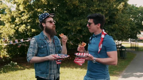Two guys having a chat while eating pizza at 4th of July party Stock Footage 133618882