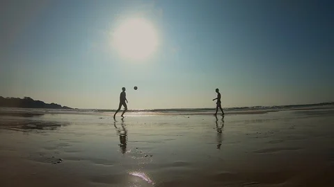 Two guys juggle a ball on the low tide beach under the warm sun Vídeos de archivo 129754665