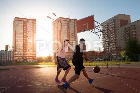 Two Guys Jump Stretch To The Ball On The Basketball Court. Backlight. Sun In The
