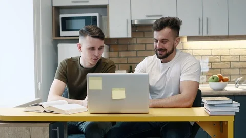 Two guys learn and work on a computer on project using a textbook sitting in the Stock-Footage 103855540