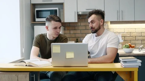 Two guys learn and work on a computer on project using a textbook sitting in the Stockbeeldmateriaal 103999479
