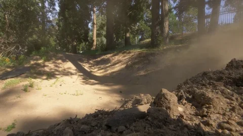 Two guys mountain biking jumps and then a steep corner, making a dust cloud. Video stock 77586214