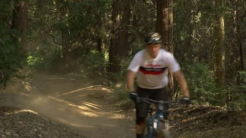 Two guys mountain biking over dirt rollers and making a dust cloud, Video stock 77586573