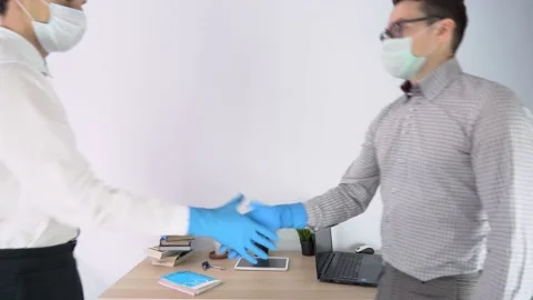 Two guys, office workers come up, greet, shake hands in blue protective gloves Video stock 131470792