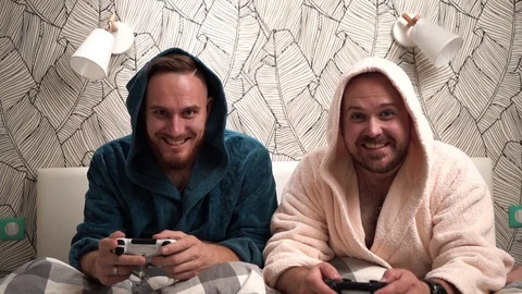 Two guys play computer games on the bed in bathrobes and win. Slow motion Stock Footage 112827311