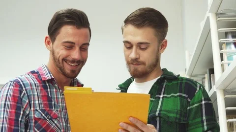 Two guys read papers in a folder and laugh Stock Footage 81928500