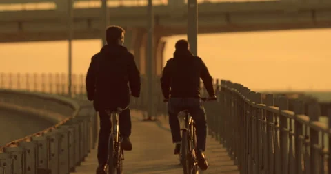 Two guys ride bicycles along the embankment of the river in the rays of sunset Stock Footage 119607035