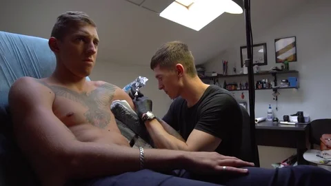 Two guys serious look one of them doing a tattoo Stock Footage 82840159