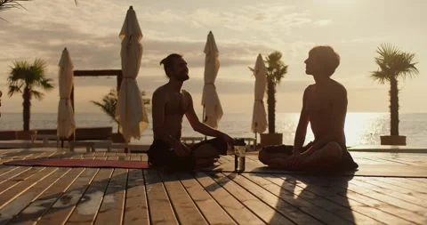 Two guys sit on mats and chat on the beach in the morning. Relax on the sunny Stock Footage 249435463