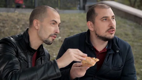 Two guys sit in the park and eat pizza with chicken and chat Stock-Footage 97799953