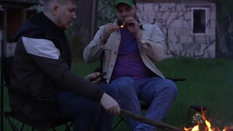 Two guys smoke in front of a fire. Stock Footage 277109956
