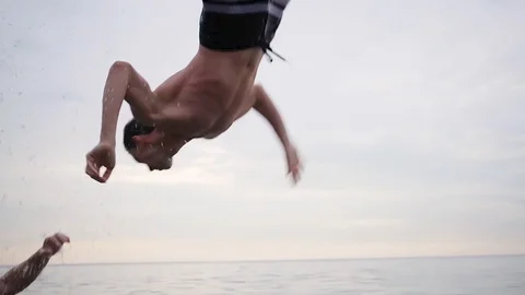 Two guys throw a third over the water and he makes a flip back and dives Video stock 90811709