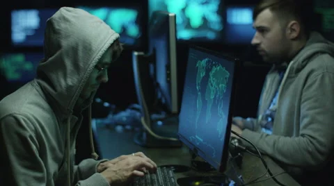 Two hackers in hoods work on a computers with maps and data on display screens Stock Footage 59156900