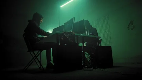 Two hackers in hoods work on a computers with maps and data on display screens Stock Footage 111286921