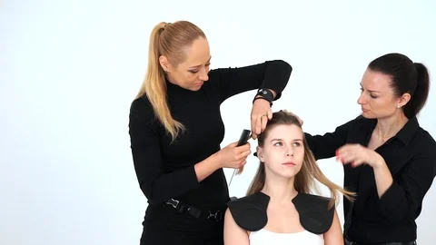 Two hairdressers at the same time doing a hairstyle for the client on a white ba Stock Footage 88876529