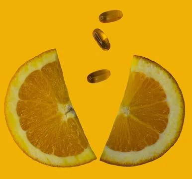 Two half of orange slice and softgel vitamins falling on yellow background. Stock Photos