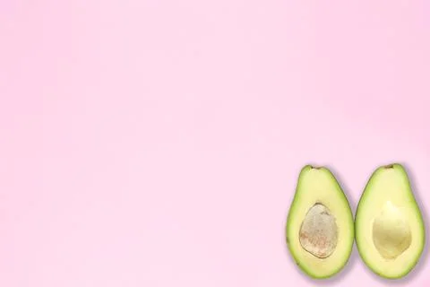 Two halfs of avocado with and without seed on pink background. Top view. Stock Photos