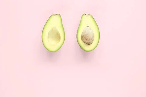 Two halfs of avocado with and without seed on pink background. Top view. Stock Photos