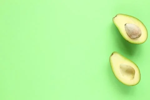 Two halfs of avocado with and without seed on green background. Top view. Stock Photos