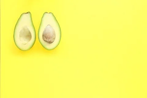 Two halfs of avocado with and without seed on yellow background. Stock Photos