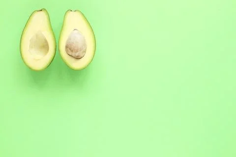Two halfs of avocado with and without seed on green background. Top view. Stock Photos