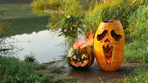 Two Halloween pumpkins are burning on the shore of the pond. Stock Footage 138124975
