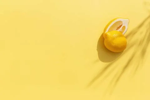  Two halved cuts of lemon with shadow from palm leaf on yellow background ... Stock Photos
