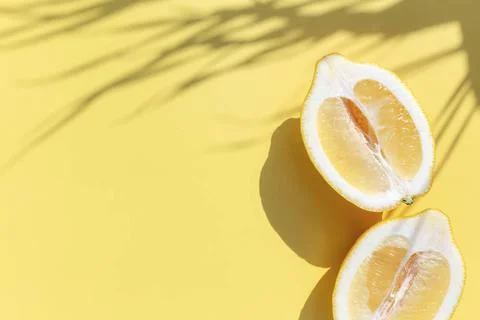  Two halved cuts of lemon with shadow from palm leaf on yellow background ... Stock Photos