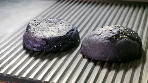 Two halves of black hamburger bun are being fried in broiler pan for burger. 4K Stock Footage 98025985