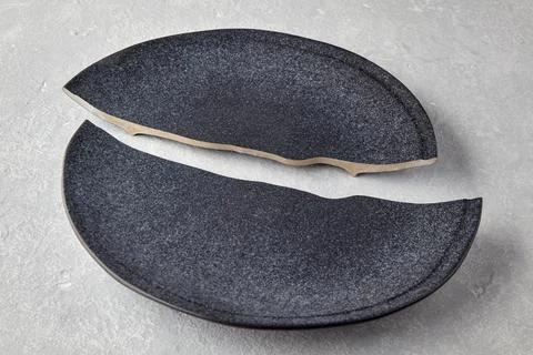 Two halves of a broken dark ceramic plate on a light gray concrete table Stock Photos