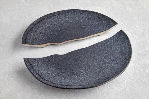 Two halves of a broken dark ceramic plate on a light gray concre Stock Photos