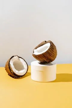 Two halves of coconut and a jar of cosmetics on a yellow and gray background. Stock Photos