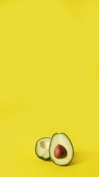 Two halves of cut avocado fruit on yellow background, vertical, 16:9 Stock Photos