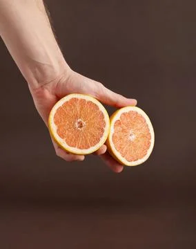 Two halves of a cut grapefruit on man's hand on a brown background. Stock Photos