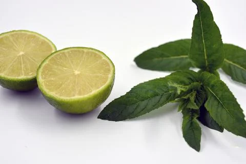 Two halves of cut lime and lime sprigs set on a white background. Stock Photos