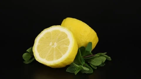 Two halves lemons and sprigs of mint rotates on a black background. Vidéo 152032802