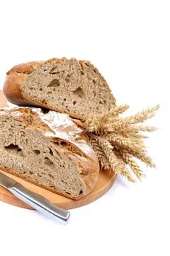 Two halves a loaf of rye bread with a knife and wheat ears. Stock Photos