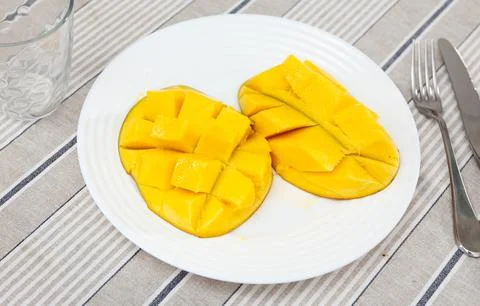 Two halves of ripe yellow mango cut into cubes lie on white round plate Stock Photos