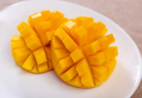Two halves of ripe yellow mango cut into cubes lie on white round plate Stock Photos
