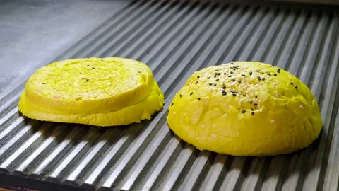 Two halves of yellow hamburger bun are being fried in broiler pan for burger. 4K Stock Footage 98025269