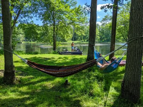 Two hammocks set up by a river with one man in the hammock and another on a boat Stock Photos