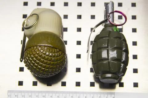 Two hand-held fragmentation metal grenades with a forensic ruler Stock Photos