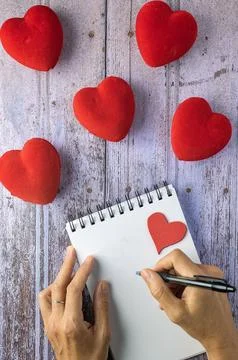 Two hands and a notepad, red hearts on a wooden board, concept of personal .. Stock Photos