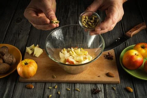 Two hands are adding spices to a bowl filled with chopped apples. Nearby are  Stock Photos