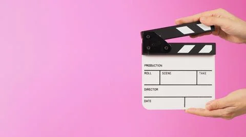 Two hands are holding a small white clapper board or movie slate on pink back Stock Photos