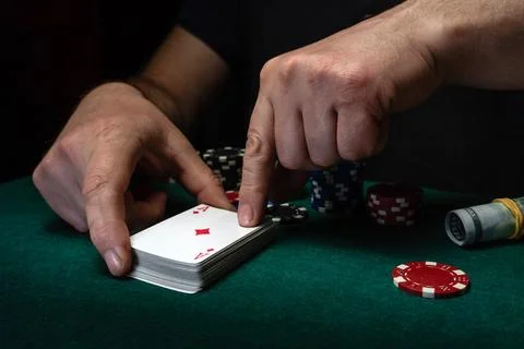 Two hands are seen arranging a stack of cards on a green table. Poker chips.. Foto stock