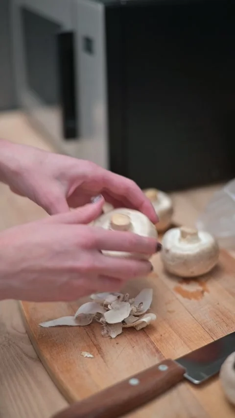 Two hands are shown removing mushroom stems and cleaning the caps on a wooden 库存影片 337112373