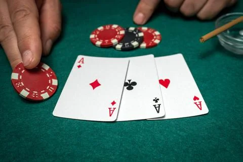 Two hands are visible, one placing a red poker chip on a table. Three playi.. Foto stock