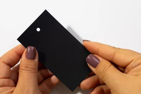 Two hands with cardboard black rectangular blank tag with little hole in upper Stock Photos